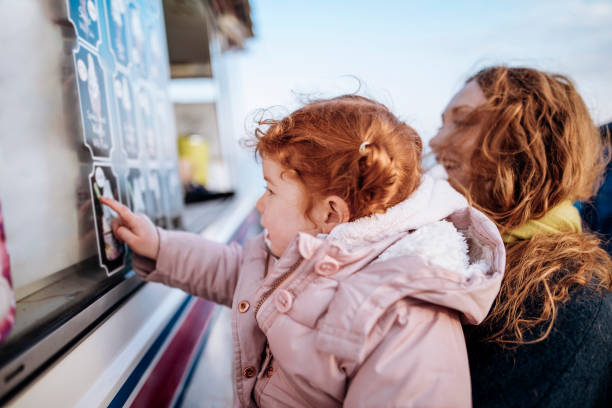 Little Redhead Girls at an Ice-Cream Van Young redheaded family stand at an ice-cream van while on the coast. Its cold outside so they are wrapped up warm. The mother holds the little girl up so she can  show her what she wants ice cream truck stock pictures, royalty-free photos & images