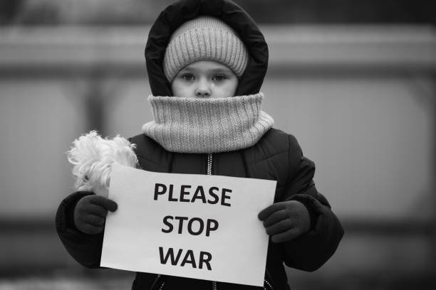 Little refugee girl with a sad look and a poster that says no to war. Social problem of refugees and internally displaced persons. stock photo