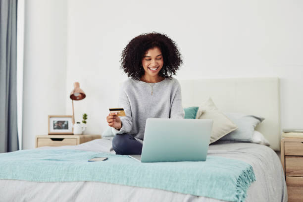 A little retail therapy never hurt anyone Cropped shot of an attractive young woman sitting on her bed at home and using her laptop for online shopping online shopping stock pictures, royalty-free photos & images