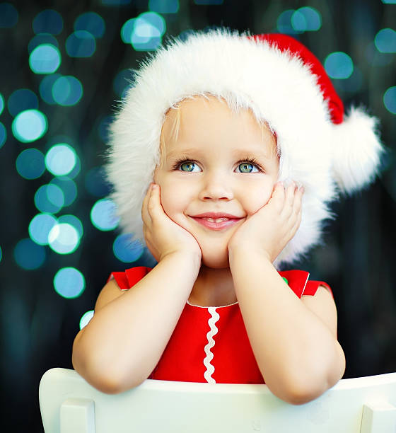 Little Santa helper A cute smiling 2-years old girl in a Santa hat and red dress against Christmas glitter close-up beautiful polish girls stock pictures, royalty-free photos & images