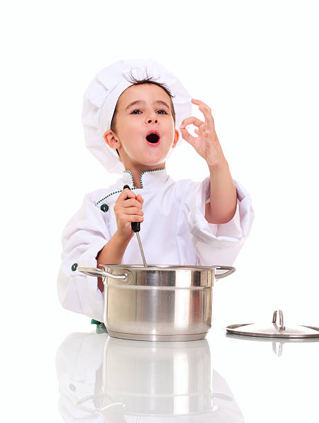 Little singing boy chef in uniform with ladle stiring pot stock photo