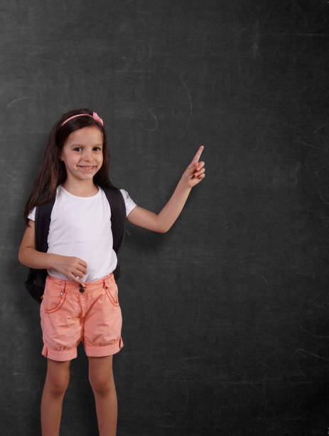 little sweet girl with backpack in front of chalkboard. back to school concept. stock photo