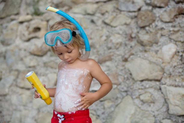 Little toddler child, holding sun cream, applying it on his body, sun protection during summer stock photo