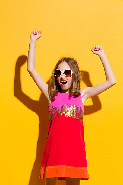 Little winner girl Happy girl in sunglasses and mini dress shouting with arms raised. Three quarter length studio shot on yellow background. girls in very short dresses stock pictures, royalty-free photos & images
