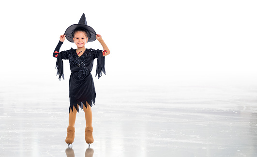 Little young skater posing in halloween witch costume on ice arena on white background