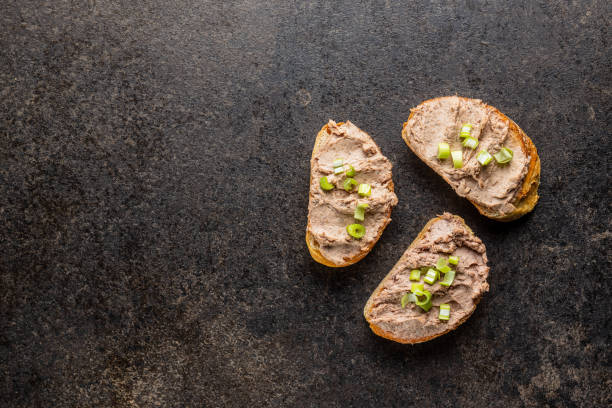 Liver pate on sliced baguette. Liver pate on sliced baguette on black kitchen table. Top view. liver pâté photos stock pictures, royalty-free photos & images