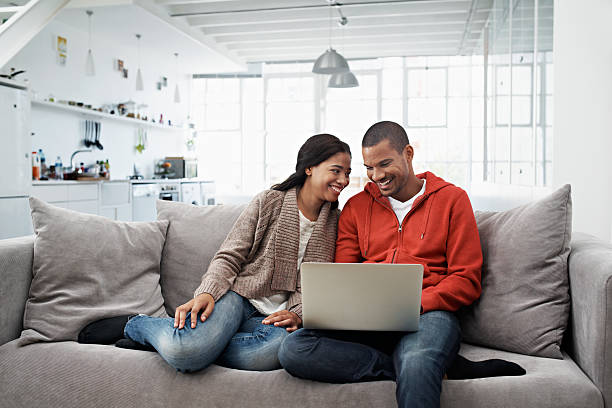 Living life wirelessly Shot of a smiling young couple sitting on their sofa using a laptop laptop couple stock pictures, royalty-free photos & images