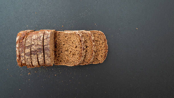 Loaf of grain bread with crumbs on black wooden surface, top view stock photo