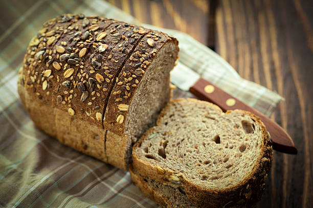 Loaf of Multigrain Bread Sliced Homemade whole grain bread on plate. Freshly baked, sunflower,sesame and pumpkin seeds are spread all over wholegrain stock pictures, royalty-free photos & images