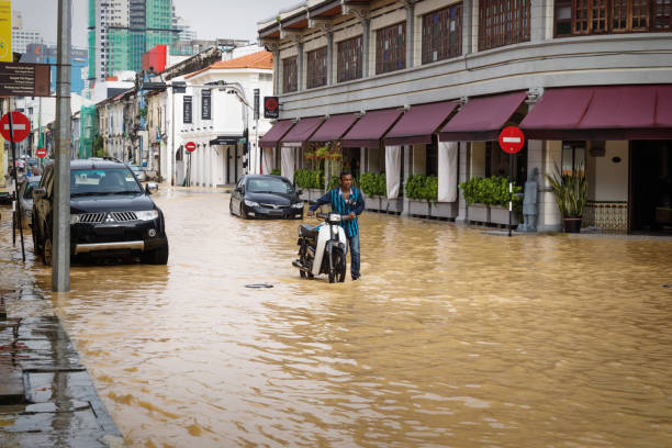 anwohner schiebt motorrad durch überflutete straße nach heftigen regenfällen in georgetown, penang, malaysia - motorrad fluss stock-fotos und bilder