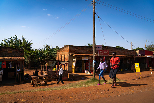 Jinja, Uganda - 24 July 2021. \nThere are settlements and shops along the road. The earth is red in color because of the large amount of iron and minerals in the earth.
