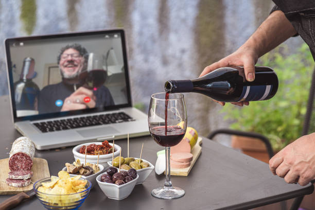 잠그기 아페리티프 화상 통화 파티. 성인 남성은 covid-19 제한 기간 동안 원격 회의 플랫폼 앱을 사용하여 집에서 스낵, 와인 및 이탈리아 전채와 함께 식사 전식대식을 만들고 있습니다. - 가상 이벤트 뉴스 사진 이미지