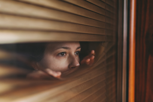 Woman at home during COVID-19 pandemic is looking through window