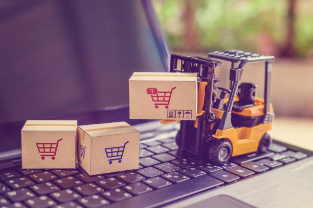 Logistics and supply chain management for online shopping concept : Fork-lift moves a box with a red shopping cart logo, 2 cartons on a laptop computer. stock photo