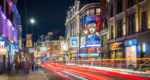 Traffic zooming along Shaftesbury Avenue past the tourist crowds and the billboards of London’s vibrant theatre district at night.