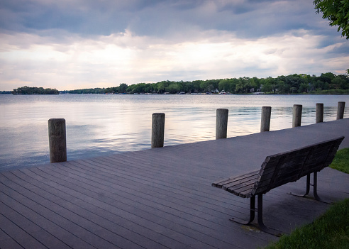 A lone bench looks out onto Pewaukee Lake in Waukesha County, Wisconsin,  on a gray, cloudy morning.