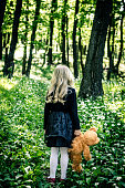lost girl in black dress holding teddy bear toy in the spring forest back view