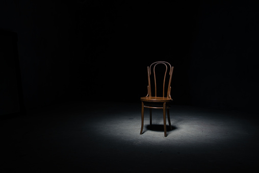 Lonely chair in the spot of light on black background at empty roomLonely chair in the spot of light on black background at empty room