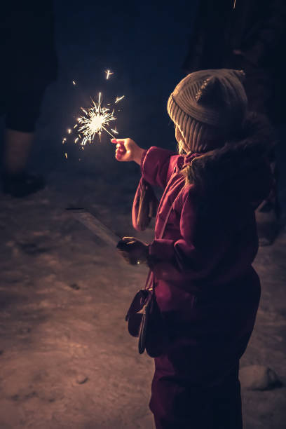 Lonely child with sparkler in the winter night standing alone in snow and lighting the way stock photo