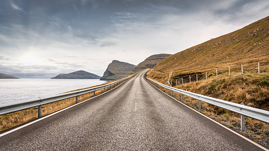 Faroe Islands Vidoy Island Lonely Empty Coastal Country National Road along the fjord hills and north atlantic ocean. Panorama of empty national country road from Norddepil - Norddeble Town on Viðoy Island under moody faroese skyscape. Norddepil - Norðdepil, Vidoy Island, Faroe Islands, Kingdom of Denmark, Nordic Countries, Europe