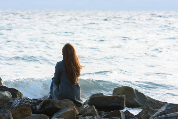 A lonely girl sits on the rocks by the sea and looks into the distance A lonely girl sits on the rocks by the sea and looks into the distance divorce beach stock pictures, royalty-free photos & images