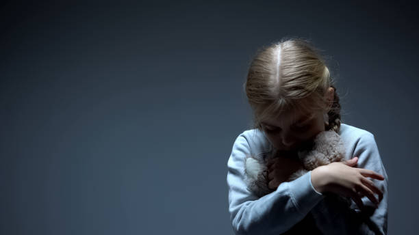 Lonely little child hugging teddy bear, bullying concept, dark background Lonely little child hugging teddy bear, bullying concept, dark background one girl only stock pictures, royalty-free photos & images