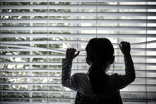 Lonely toddler child standing in front of a window looking outside