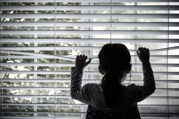 Lonely little kid in front of a window stock photo