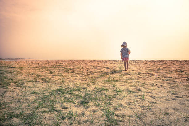 Lonely lost child toddler standing alone in sand dunes exploring childhood travel lifestyle stock photo
