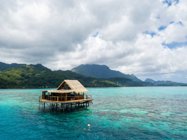 Lonely overwater bungalow of black pearl farmers. Blue azure turquoise lagoon with corals. Emerald Raiatea island, French Polynesia, Oceania. stock photo