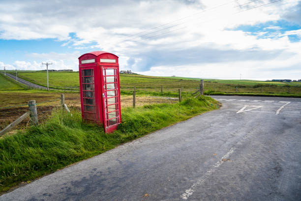 Lonely roadside red telephone booth near a road junction in the countryside Lonely traditional Bristish red telephone booth near a road junction in the countryside on a partly cloiudy spring day. Orkney Islands, Scotland, UK. red telephone box stock pictures, royalty-free photos & images