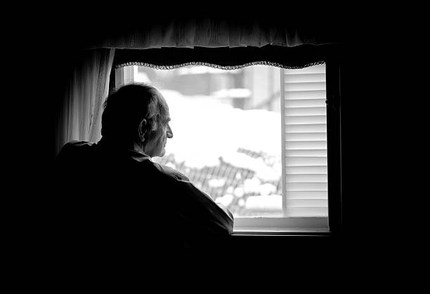 Lonely senior man looking at the window stock photo