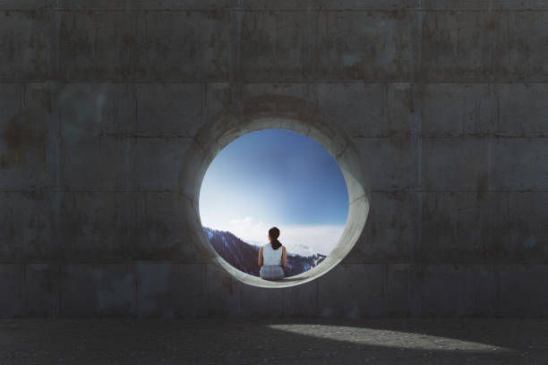 Lonely young woman sitting and looking through concrete window stock photo
