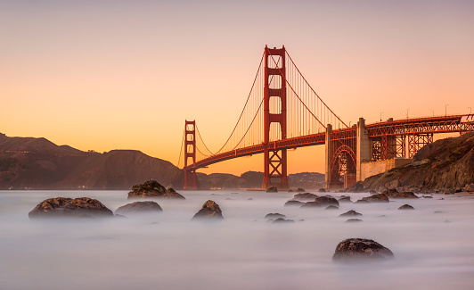 Long exposure photo in Marshall's Beach with Golden Gate Bridge in the background in San Francisco at sunset, California