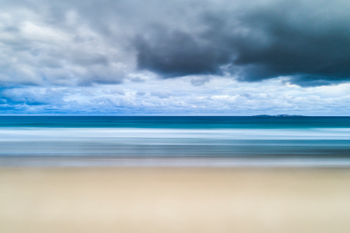 Long exposure of bright coastal beach horizon scene with storm clouds