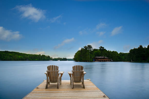 Long exposure of two empty Adirondack chairs sitting on a wooden dock stock photo