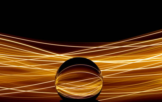 Long exposure photograph of neon gold colour in an abstract swirl, parallel lines pattern against a black background with reflections in a glass orb sphere. Light painting photography. Light painting, long exposure photograph of fairy lights reflected in a glass orb paint neon color neon light ultraviolet light stock pictures, royalty-free photos & images
