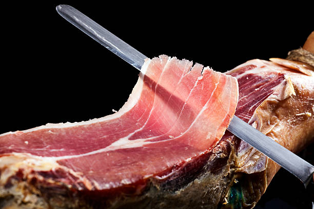 Long knife cutting into a piece of prosciutto Delicious Italian ham.  prosciutto stock pictures, royalty-free photos & images
