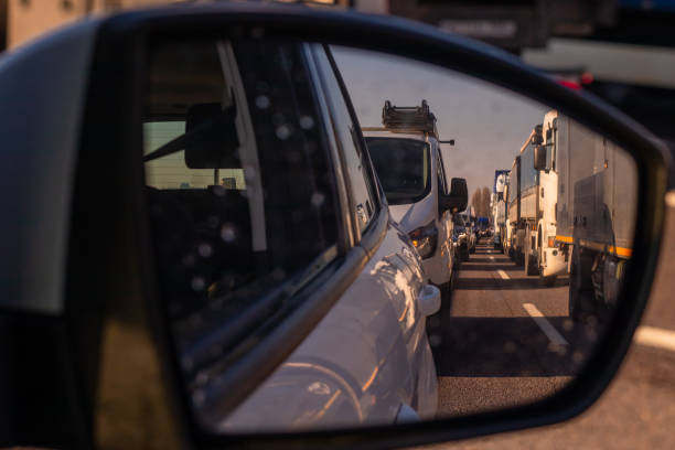 Long queue of trucks and cars as part of a traffic jam on a motorway in italy, europe on a sunny day.  Looking through rear view mirror. stock photo