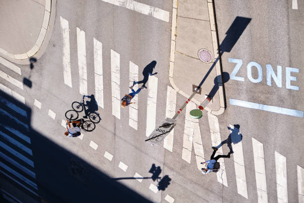 Long shadows of people walking and biking at an intersection - aerial view. stock photo