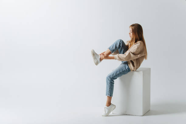 Longshot of a teenage girl lacing her sneakers. Sitting on a white cube stock photo