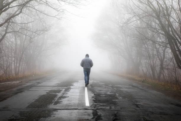 Lonly man  walk away into the misty foggy road in a dramatic mystic scene. Guy walking in a foggy autumn landscape stock photo