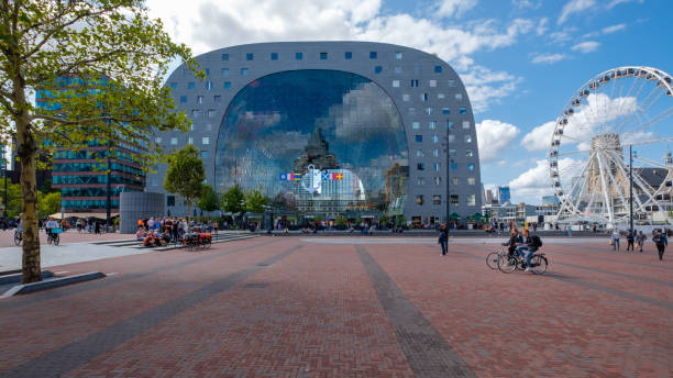 Look through from the outside of the market hall in Rotterdam. A ferris wheel next to the building and  people and cyclists on the square. stock photo