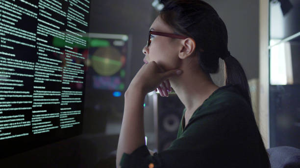 Stock photo of a young Asian woman looking at see through data whilst seated in a dark office