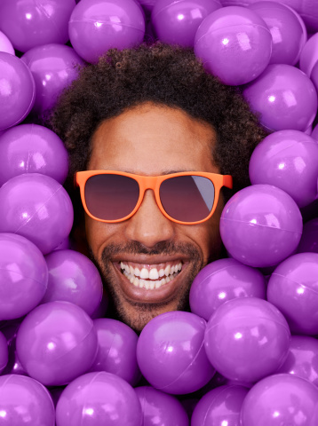 A young black man's face amongst purple pit balls