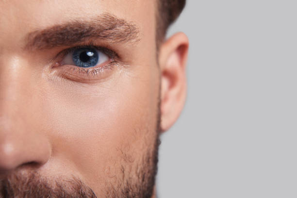 Looking deeply into your heart. Close up of good looking young man half face looking at camera while standing against grey background male skin care stock pictures, royalty-free photos & images