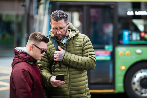A medium selective focus of a father and his teenage son who has Down Syndrome looking at a smart phone and navigating themselves aroundd the city centre of Newcastle upon Tyne in the North East of England.