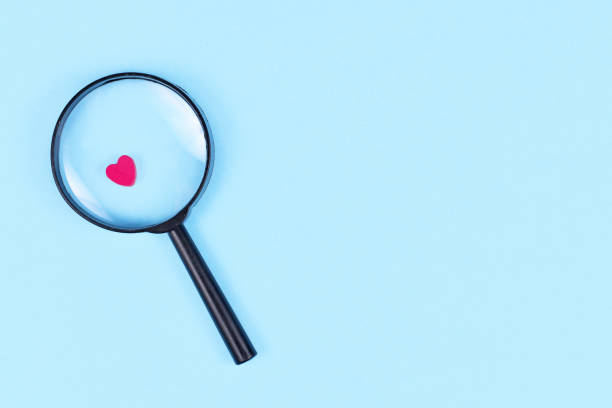 Looking for love concept with magnifier glass and pink heart icon on blue background stock photo