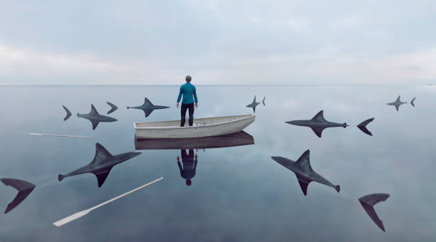 Man lost at sea in row boat made of wood. He has lost the oars and cannot sail the boat. Sharks are moving in on him. He stands up in the boat looking for a way out. Concept of failure and trying to find a solution to an emerging problem. 
Note: The man is a 3D-render. Property release attached.