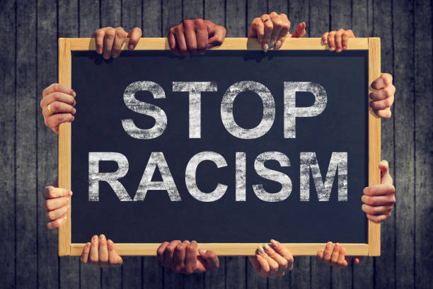 A lot of hand are holding a banner with text " Stop racism" on dark background. Different people express one common opinion Stop Racism A lot of hand are holding a banner with text " Stop racism" on dark background. Different people express one common opinion Stop Racism anti racism stock pictures, royalty-free photos & images